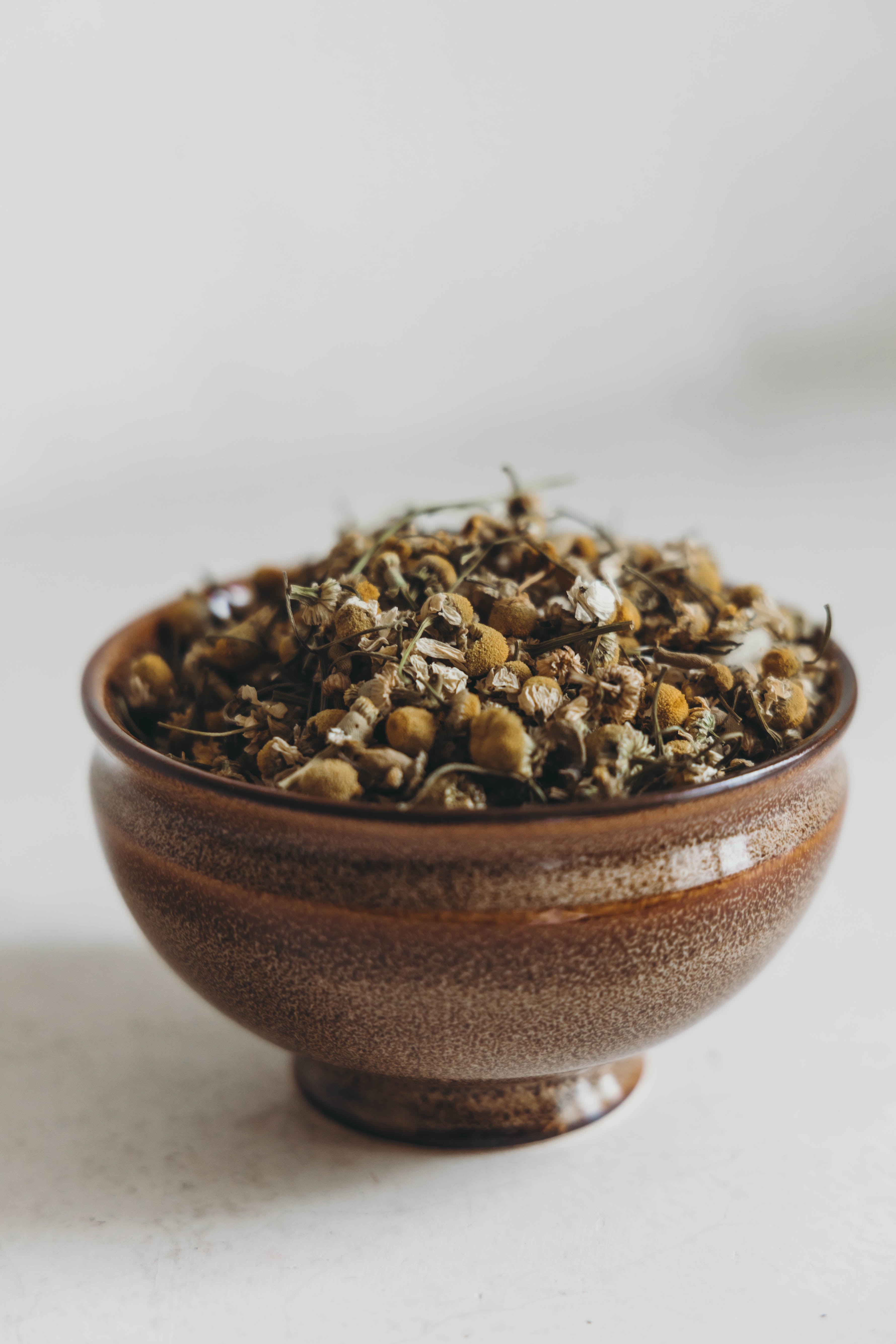 Brown ceramic bowl filled with dried herbs on a light background. Additional Benefits:
Eases anxiety
Improves sleep quality
Promotes a more calm, relaxed state
Boosts the immune system
Directions:
Bring 12 oz of water to a boil & add one teaspoon of Chamomile Tea.