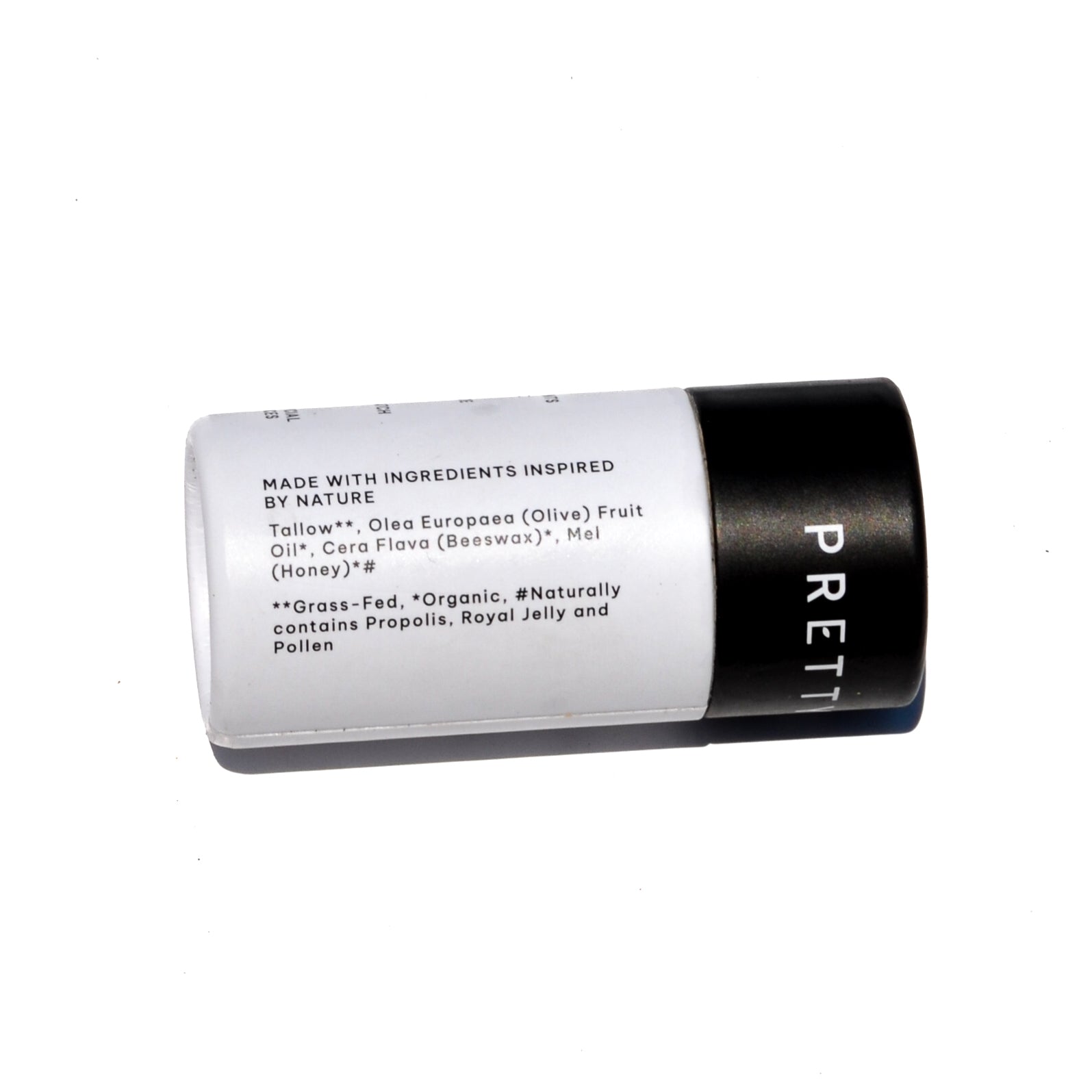 A white lip butter stick labeled 'TALLOW + HONEY' stands on a rustic wooden surface beside a black cap and honeycomb, with a burlap cloth and blurred outdoor field background. grass fed lip balm pretty farm girl handmade skin organic plastic free dry cracked lips repair comfrey