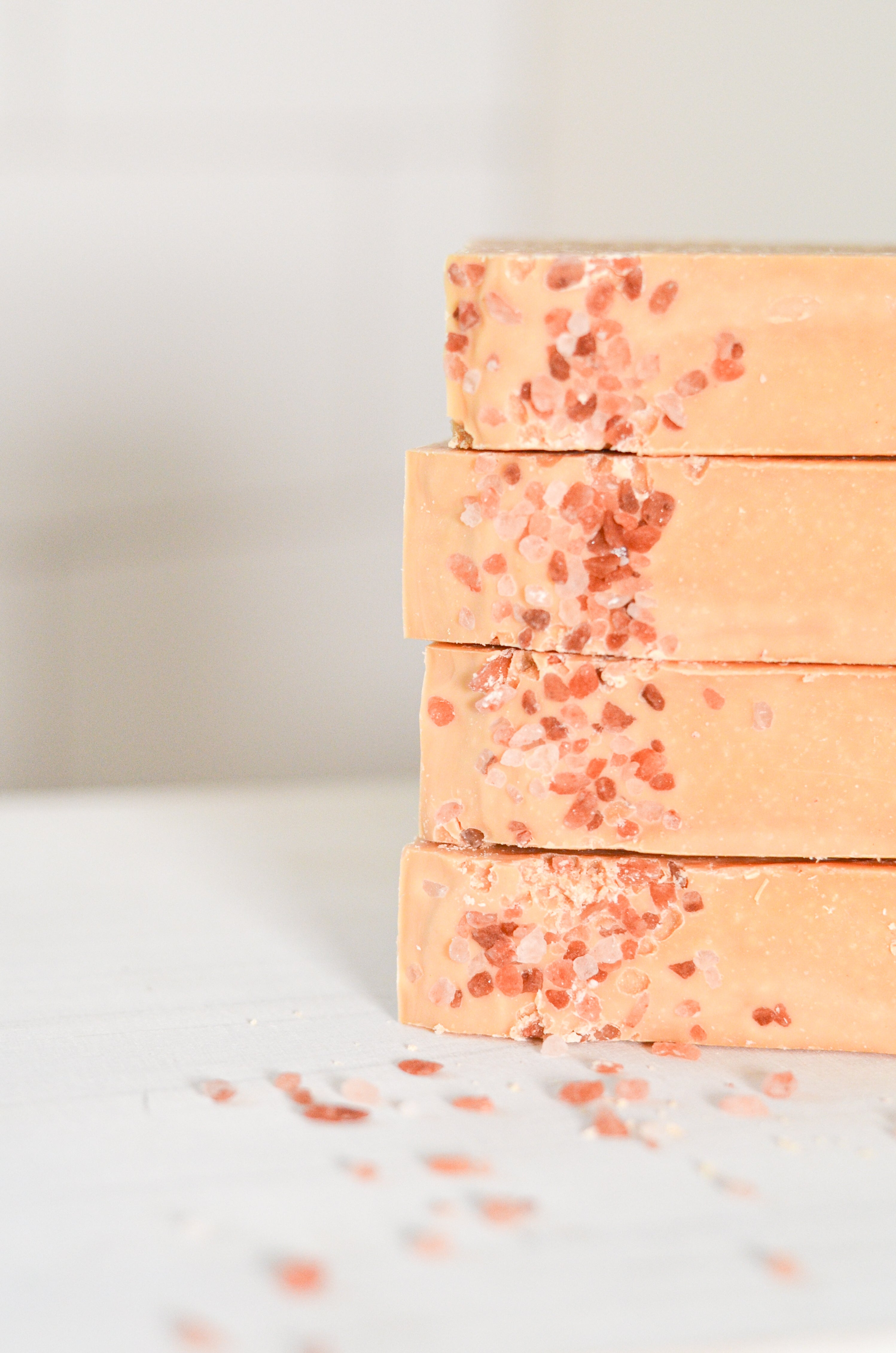 Stack of peach-colored soap bars with red specks on a light background, tallow grass fed soap for organic facial skin care. goats milk