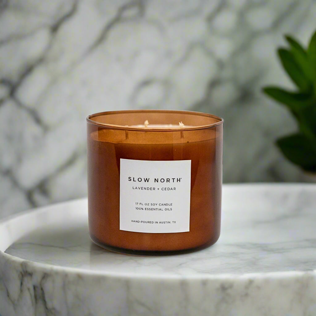 Candle with a label on a marble surface. Transform your space into a serene retreat with our new Signature 3-Wick Candle in Lavender + Cedar—a calming, grounded blend designed to fill larger spaces with soft, natural fragrance and a warm, even glow. Topped with a black metal lid.
Hand-poured in Austin, Texas, this candle is crafted with 100% soy wax and pure essential oils, offering a clean, non-toxic burn you can feel good about.