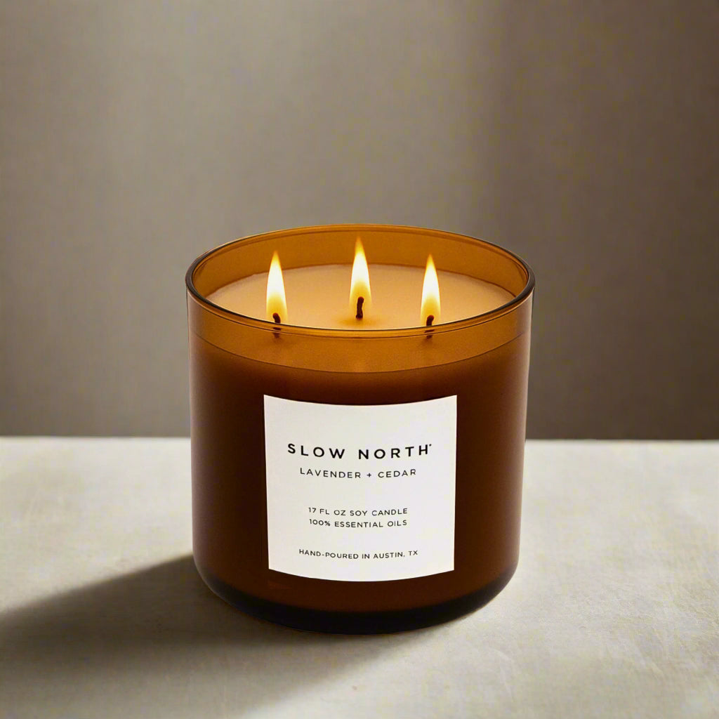 Lit candle in a brown jar with a label on a neutral background. Transform your space into a serene retreat with our new Signature 3-Wick Candle in Lavender + Cedar—a calming, grounded blend designed to fill larger spaces with soft, natural fragrance and a warm, even glow. Topped with a black metal lid.
Hand-poured in Austin, Texas, this candle is crafted with 100% soy wax and pure essential oils, offering a clean, non-toxic burn you can feel good about.