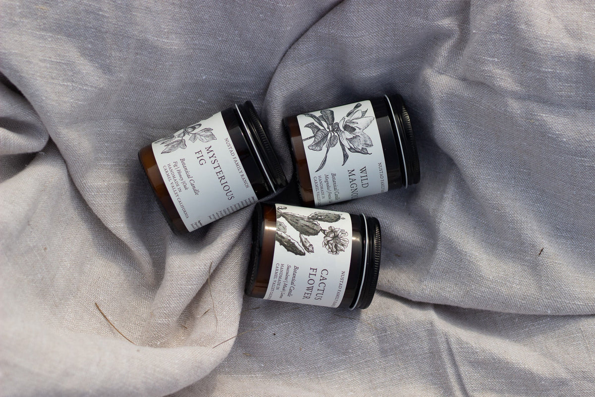 Close-up of Mysterious Fig and Wild Magnolia candle jars showing their illustrated labels.