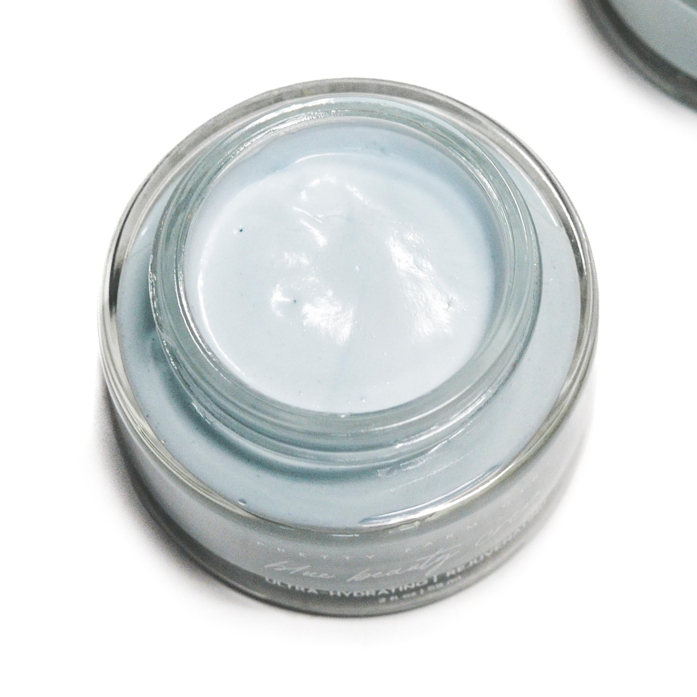 Small glass jar with a white cream inside on a white background. Skincare jar with a blurred natural background. organic natural facial moisturizer and skin nourishing with probiotics and vitamin c tallow blue tansy