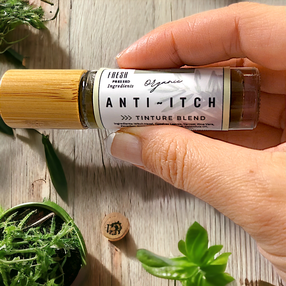 Hand holding an Anti-Itch Tincture Blend bottle horizontally, showing the label against a wooden surface.