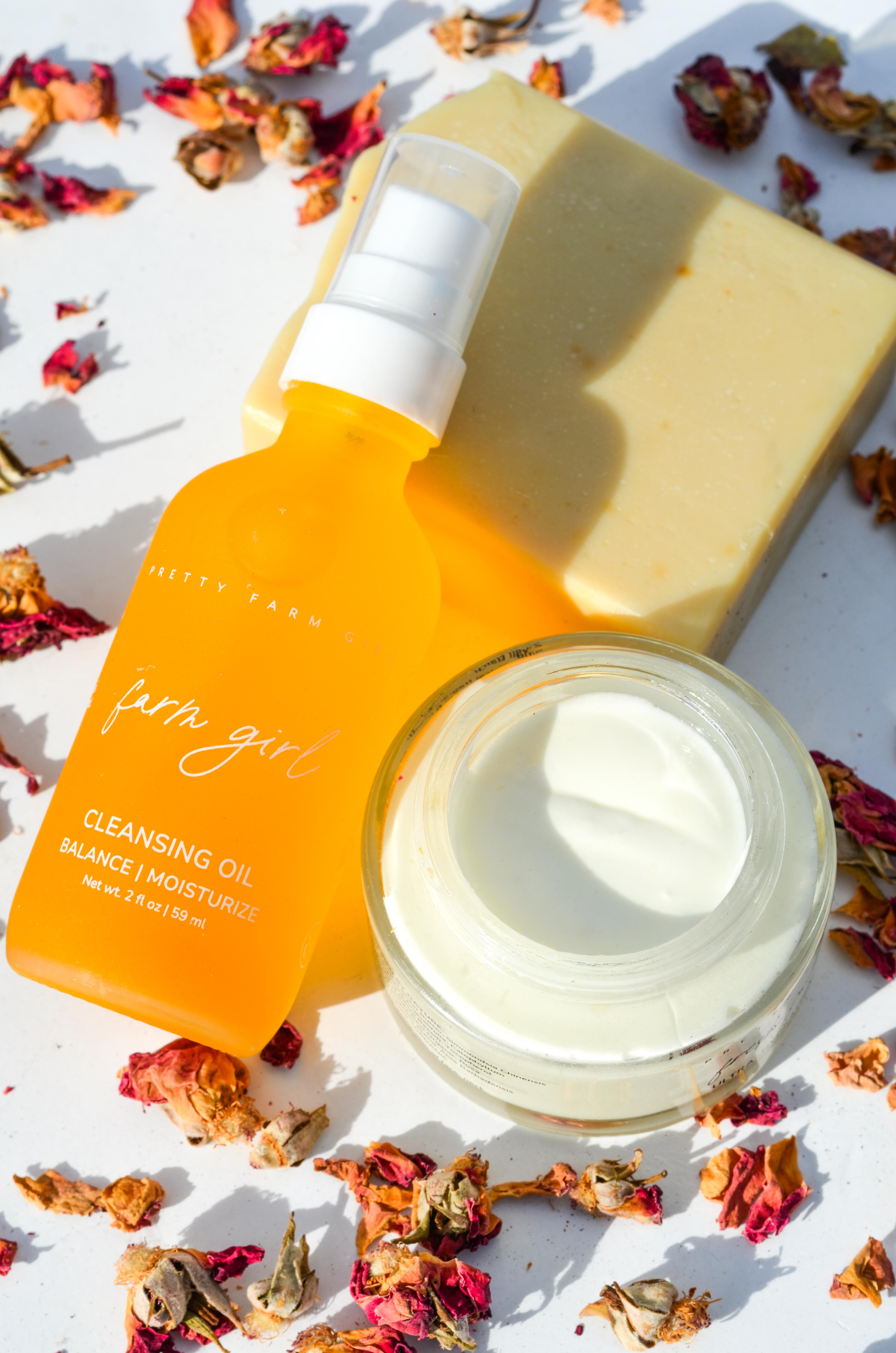 Skincare products including a bottle, jar, and bar on a white surface with dried flowers. Orange bottle and jar of facial product on a white background. rosehip and rose essential oils serum and facial cleansing lotion