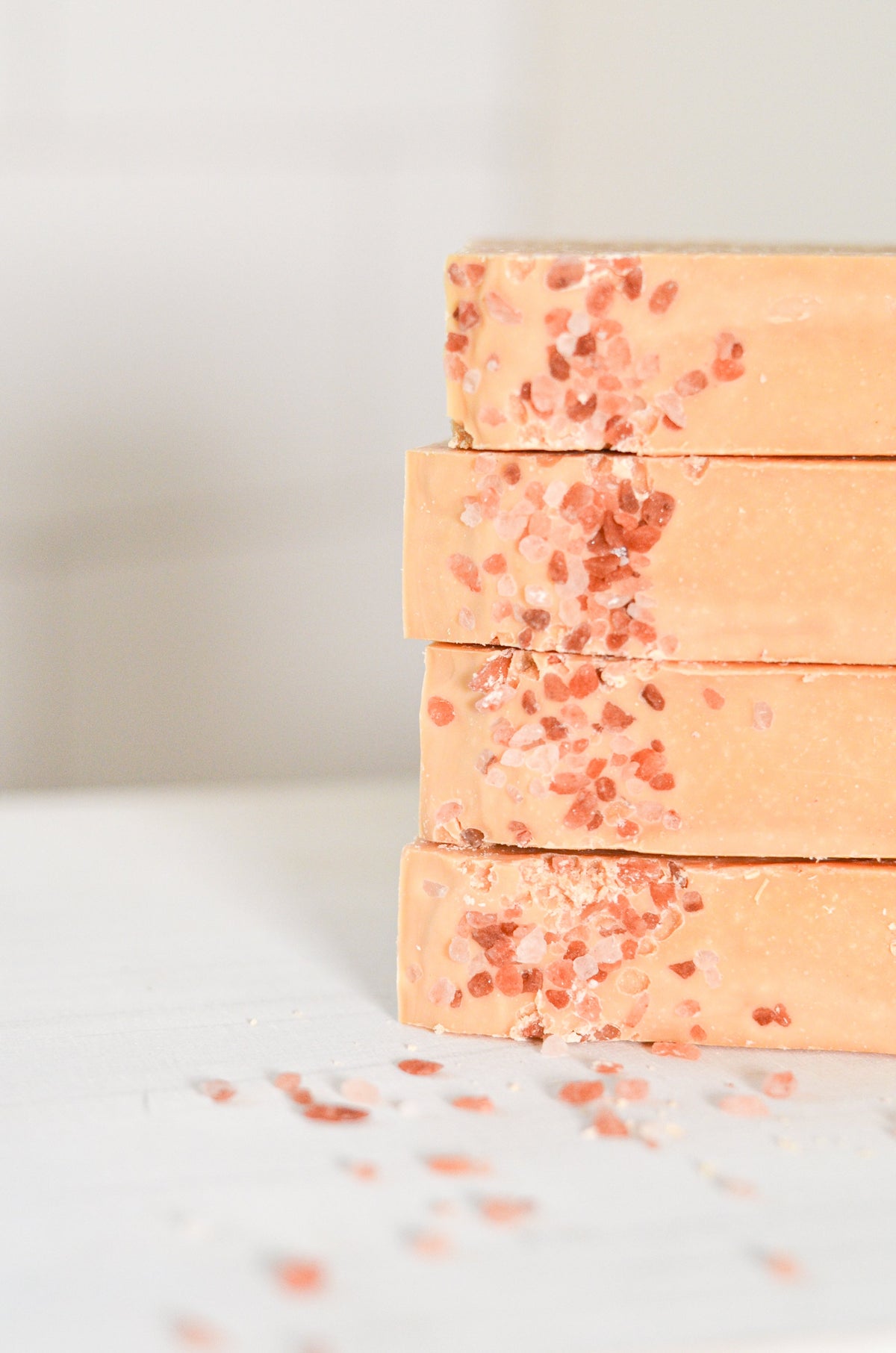 Stack of peach-colored soap bars with red specks on a light background, tallow grass fed soap for organic facial skin care. goats milk