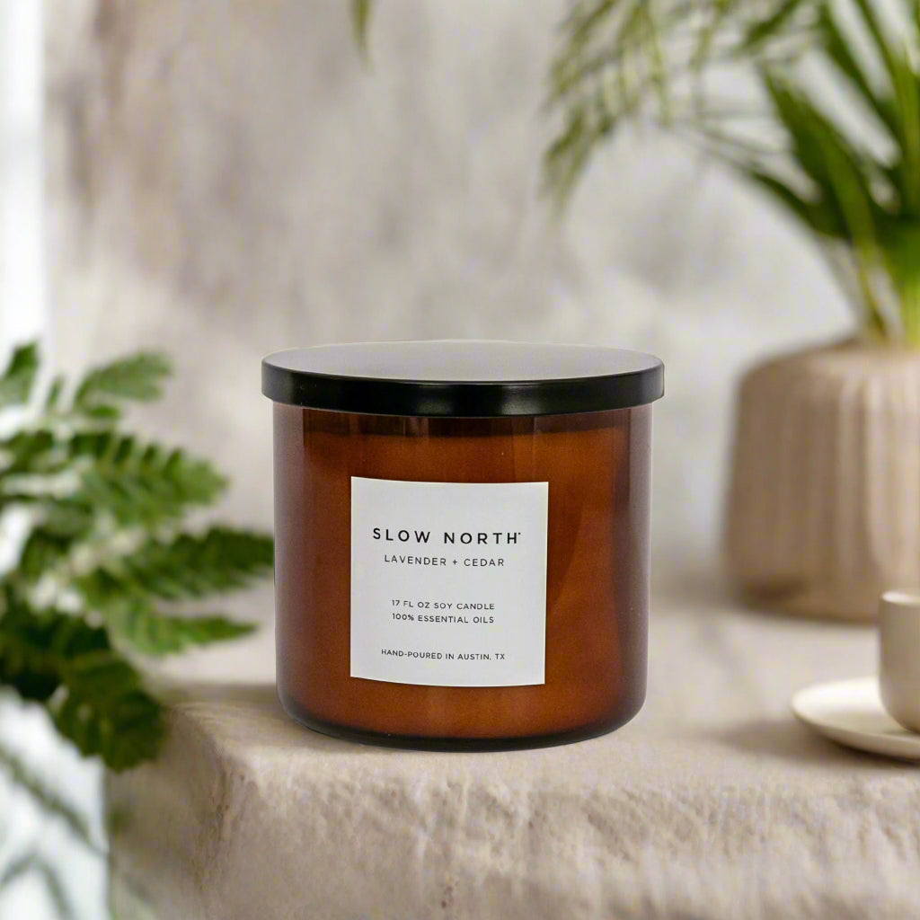 Candle with 'Slow North' label on a surface with plants in the background. Transform your space into a serene retreat with our new&nbsp;Signature 3-Wick Candle in Lavender + Cedar—a calming, grounded blend designed to fill larger spaces with soft, natural fragrance and a warm, even glow. Topped with a black metal lid.

Hand-poured in Austin, Texas, this candle is crafted with 100% soy wax and pure essential oils, offering a clean, non-toxic burn you can feel good about.