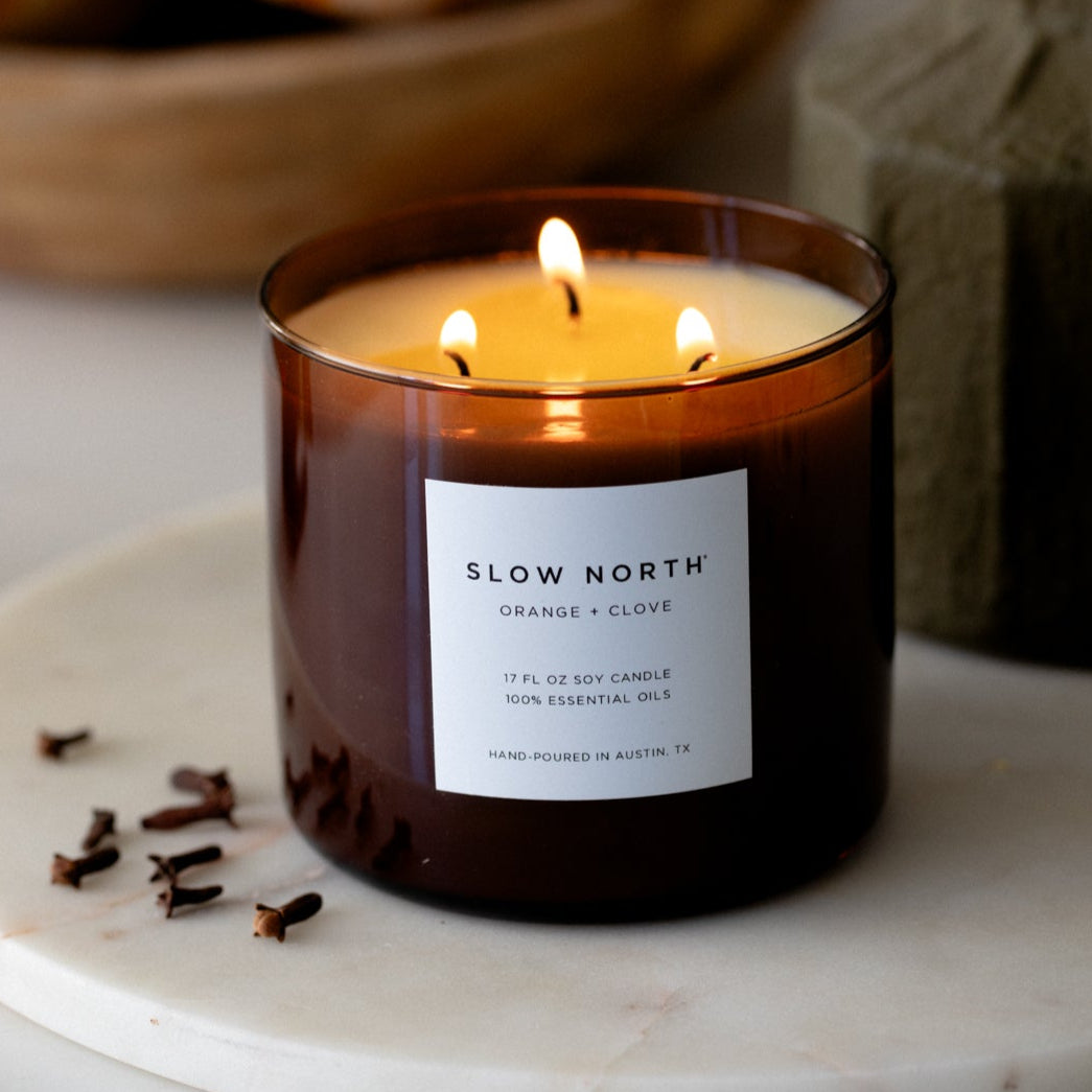 Lit candle in a glass jar with 'Slow North' label on a marble surface. SSF Organics Natural beeswax candles with essential oils holiday scents organic holistic relaxing 
