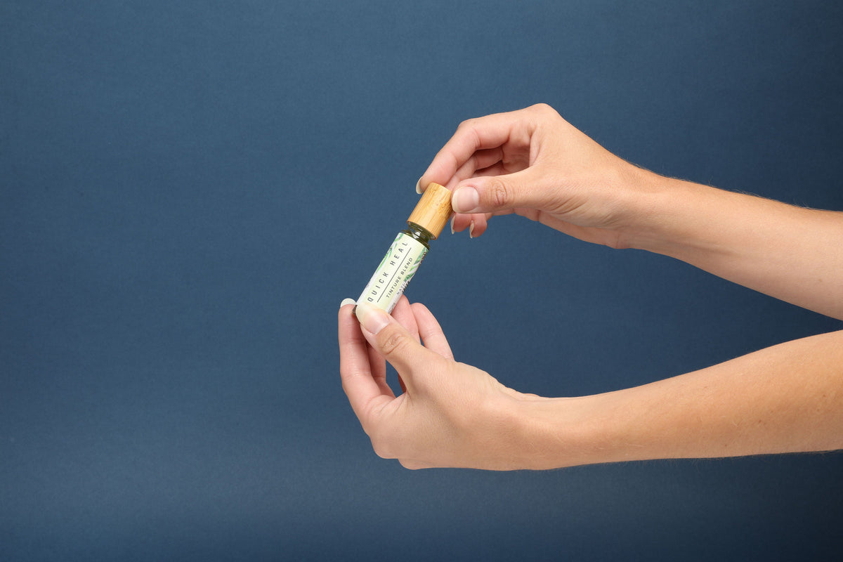 Hands holding a small bottle of SSF Organics Quick Heal Tincture Blend against a blue background