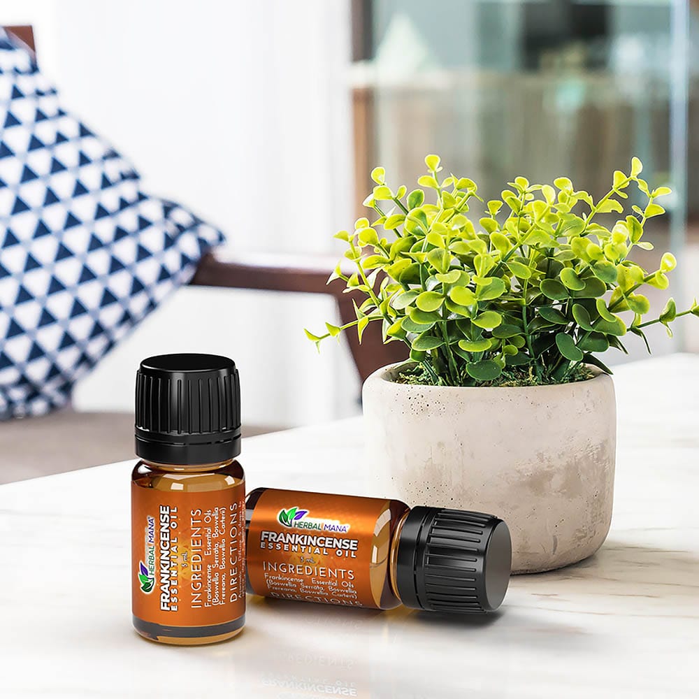 Two Herbal Mana Frankincense Essential Oil bottles, one upright and one on its side, beside a potted green plant.
