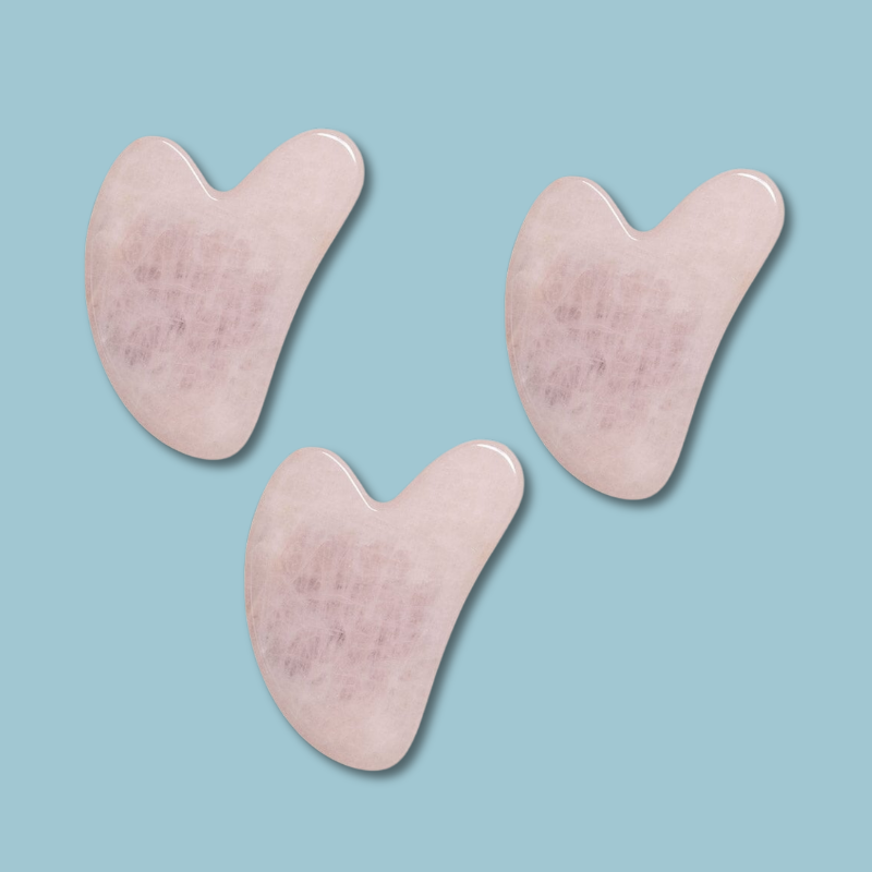 Three pink gua sha tools on a light blue background. lymph support and face treatment under eye serum with copper peptides and vitamin c