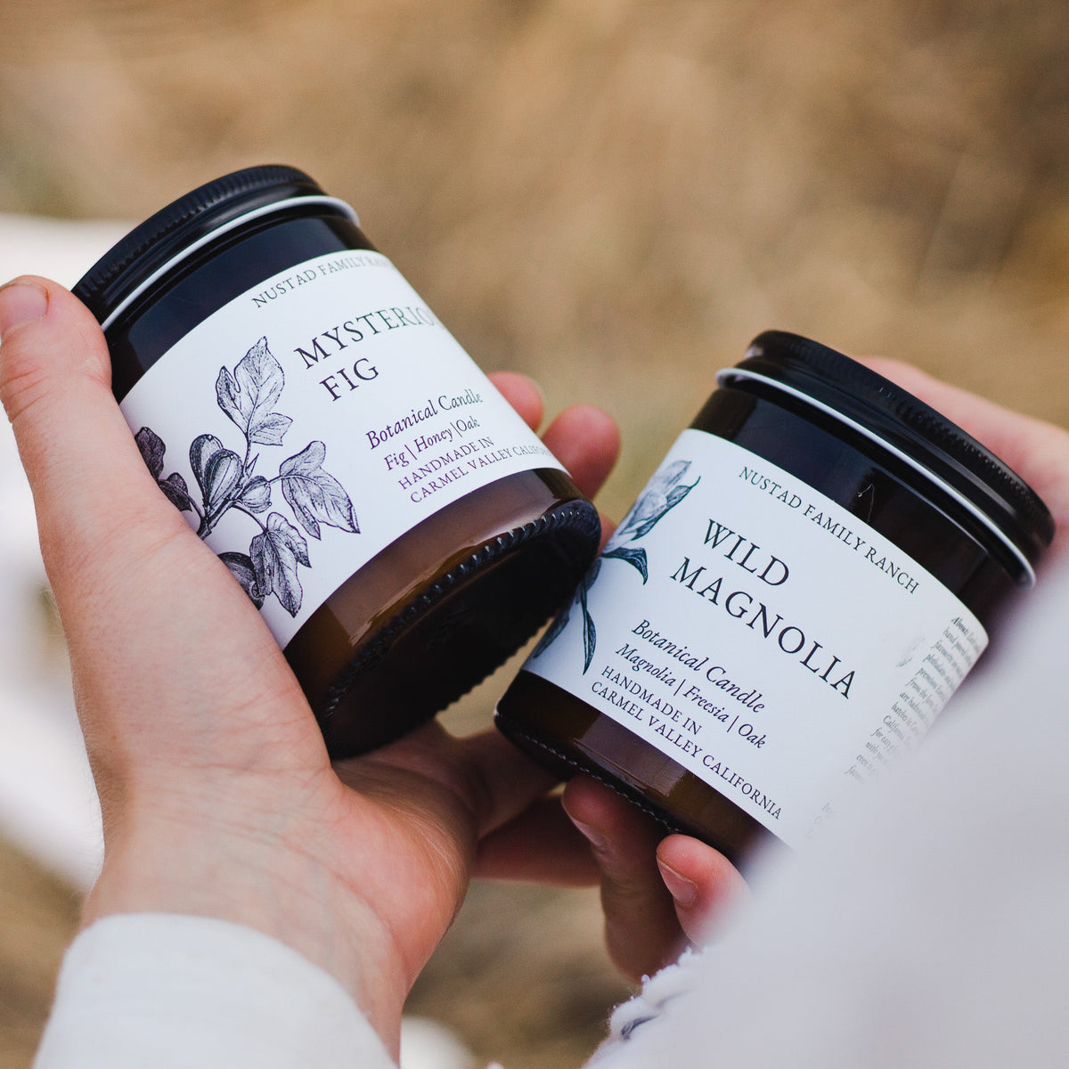 Hand carrying a Wild Magnolia amber jar candle with a black lid and illustrated botanical label.