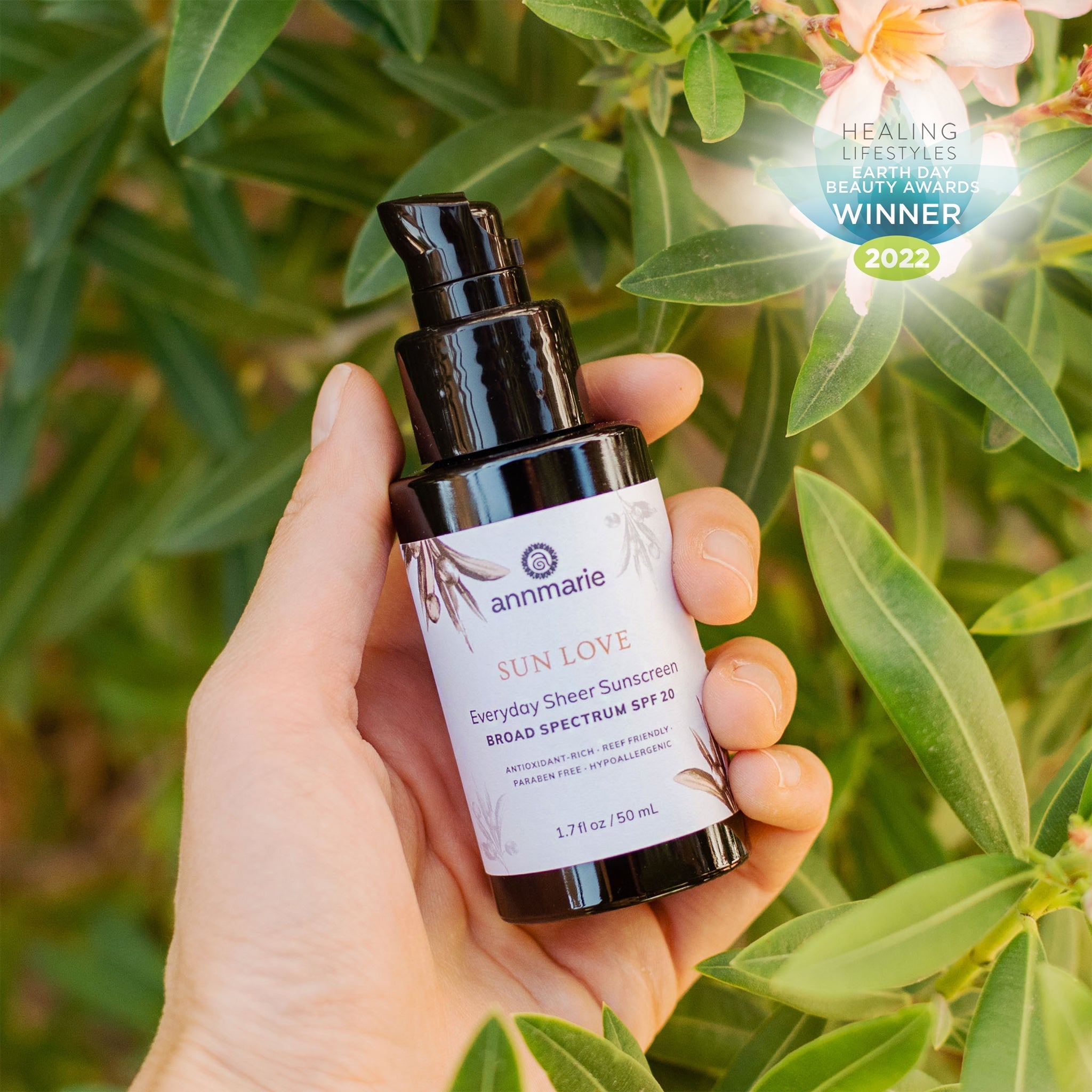 Hand holding a bottle of 'Sun Love' sunscreen with green foliage in the background. natural skin face sunscreen. comfrey and arnica tallow