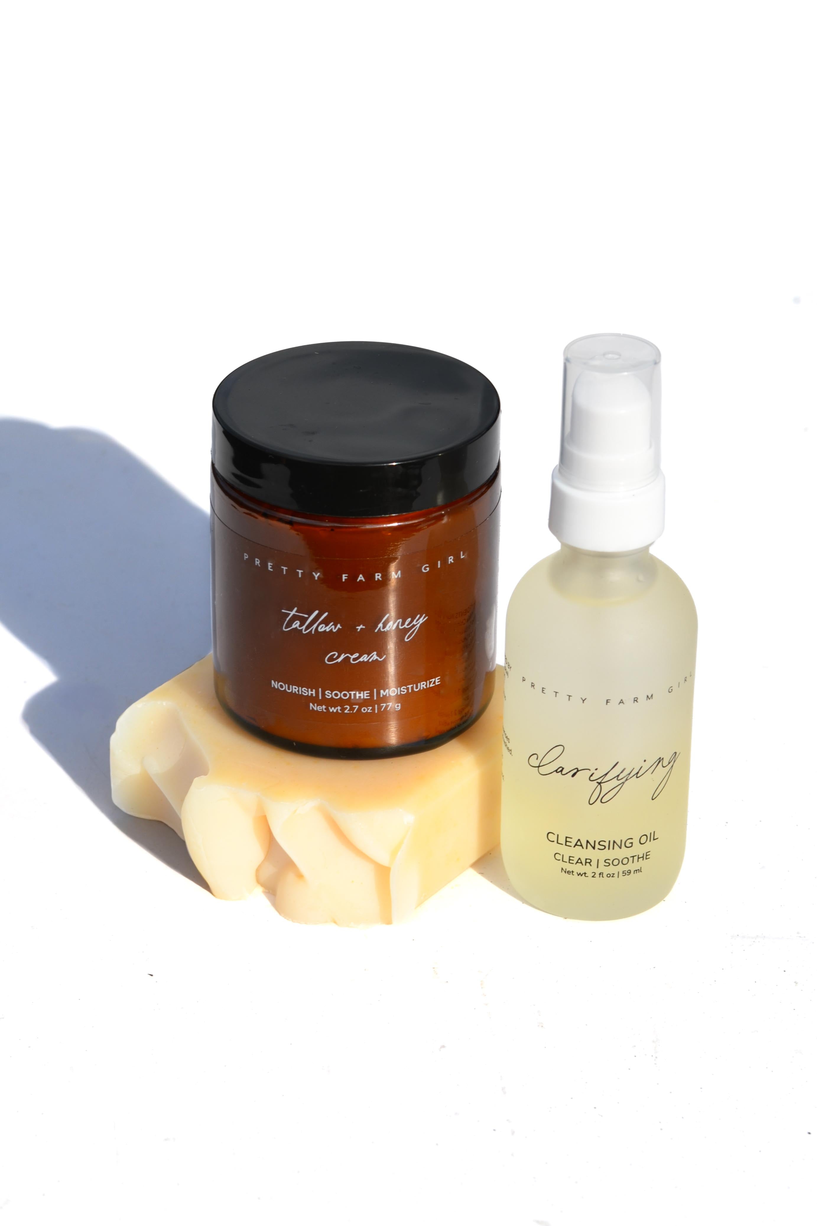 Two skincare products, a jar and a bottle, on a white background with a soft shadow. tallow arnica calendula tea tree pretty farm girl facial care organic soap serum and lotion 