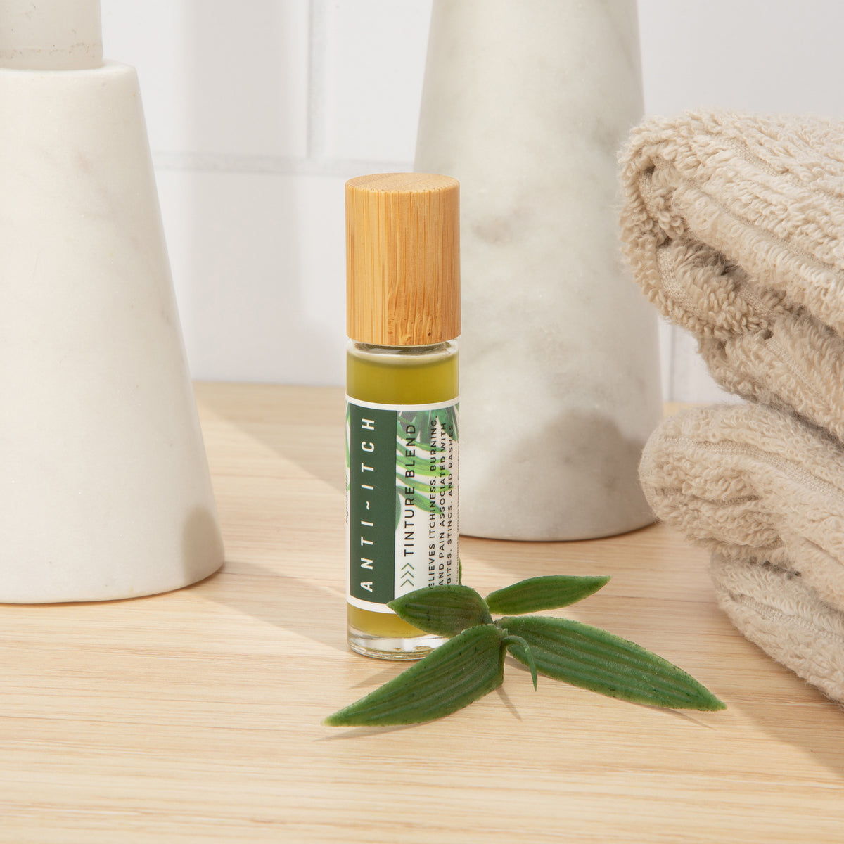 Anti-Itch Tincture Blend bottle on a bathroom counter beside green leaves, folded towels, and white containers